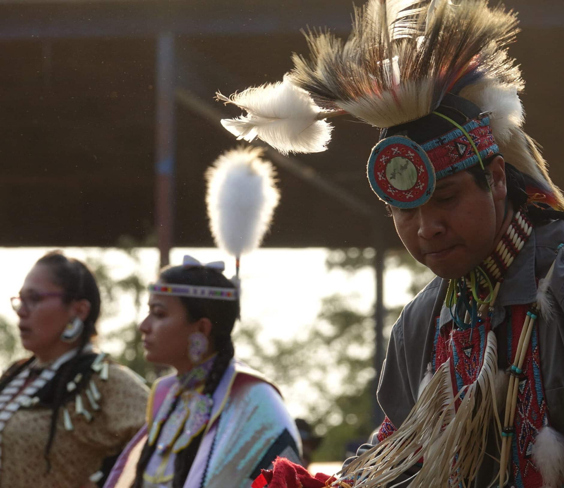 Three people in traditional First Nations regalia standing outdoors