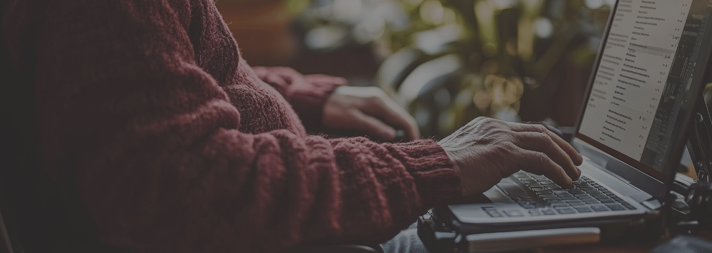 A person wearing a red jumper types on a laptop, researching law enforcement technology, with plants and natural light visible in the background.