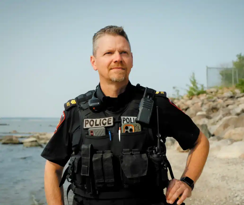 Victoria Beach Police Service officer in uniform on a Lake Manitoba shoreline, featured in FSET's ConnectedOfficer® promotional video showcasing managed IT services and the Private Community Cloud for Law Enforcement (PCCLE).